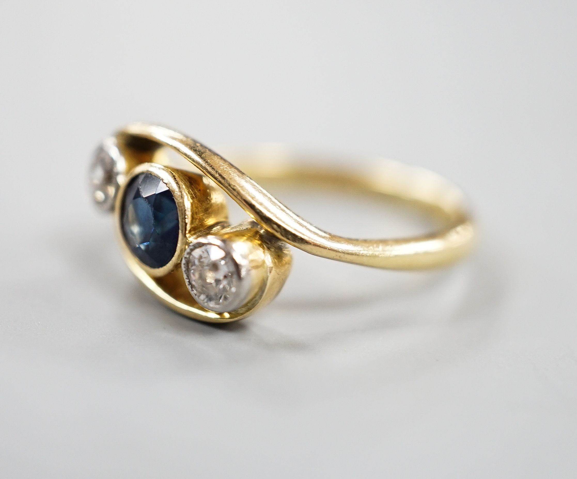 A modern 18ct gold, single stone diamond and two sapphire set crossover ring, size K, gross 3.2 grams.